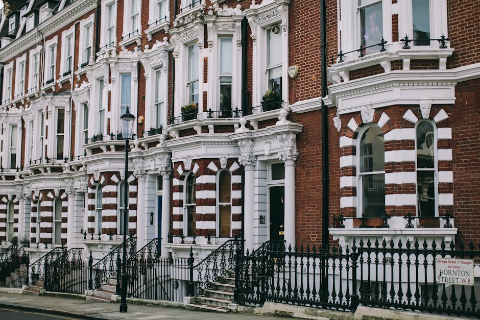 The image depicts a row of traditional Victorian terraced houses constructed from light brown and beige brickwork, with arched sash windows and white-painted window frames arranged uniformly along the